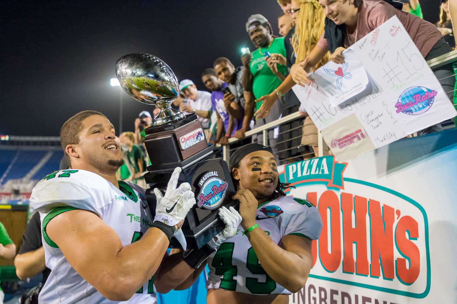 Running back Devon Johnson and linebacker Cortez Carter of the Thundering Herd hold the Boca Raton Bowl trophy in front of their cheering fans. 