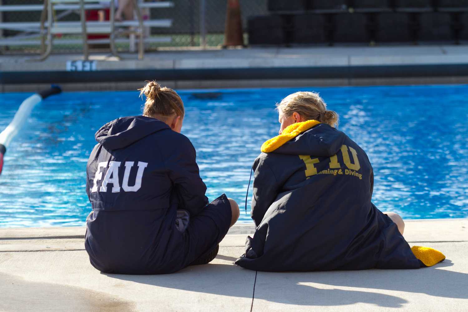 Two swimmers from FAU and FIU sit aside the pool during a break in the meet. 
