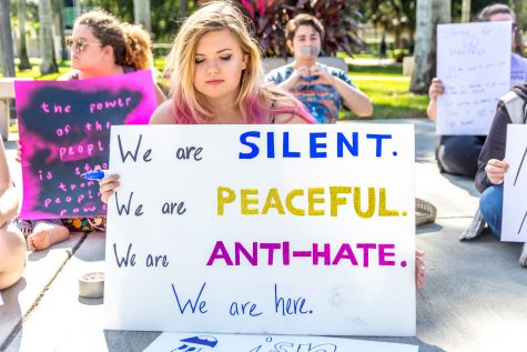Natasha Roberts a sophomore Communications major sits with the group of protesters holding a sign signalling the message of their goal: a silent, peaceful, anti-hate protest. Alexis Hayward | Contributing Photographer 