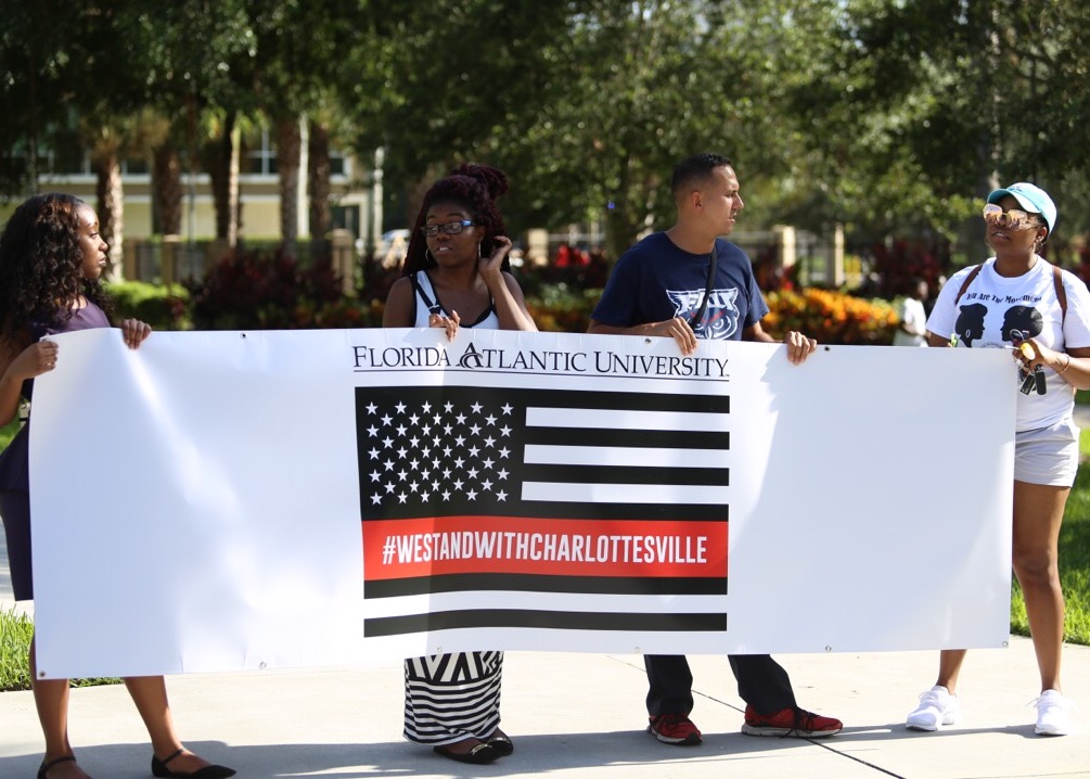 Students hold a banner before the march for Charlottesville in front of the Social Science Building. From left to right: student body Governor DerResha Bastien, Jordan Bowles, and Marek Madro. Alexander Rodriguez | Photo Editor
