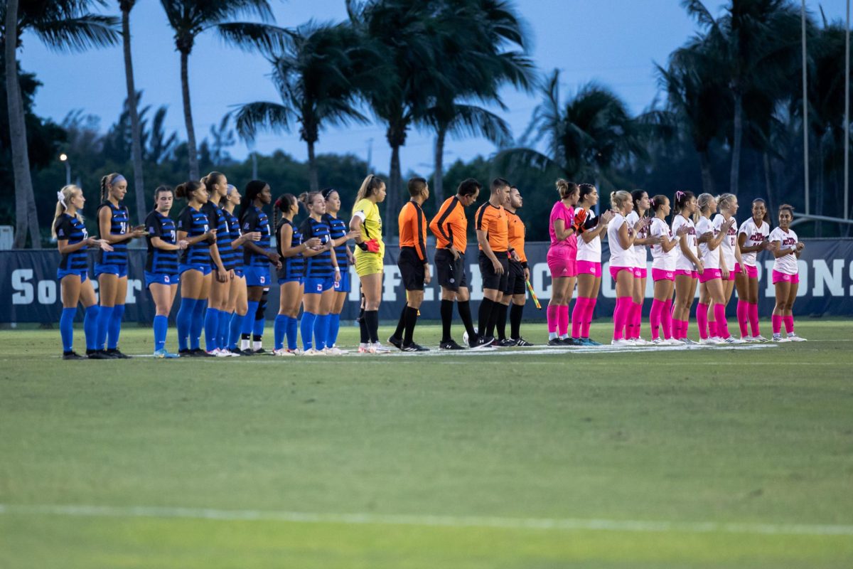 SMU (blue) and FAU (white) womens soccer teams standing for the national anthem before FAUs 2-0 loss to SMU. October 12, 2023.