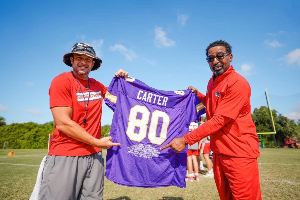 FAU head coach Tom Herman (left) and Cris Carter (right) posing with a commemorative Vikings jersey Carter presented to Herman in front of the team during practice.
