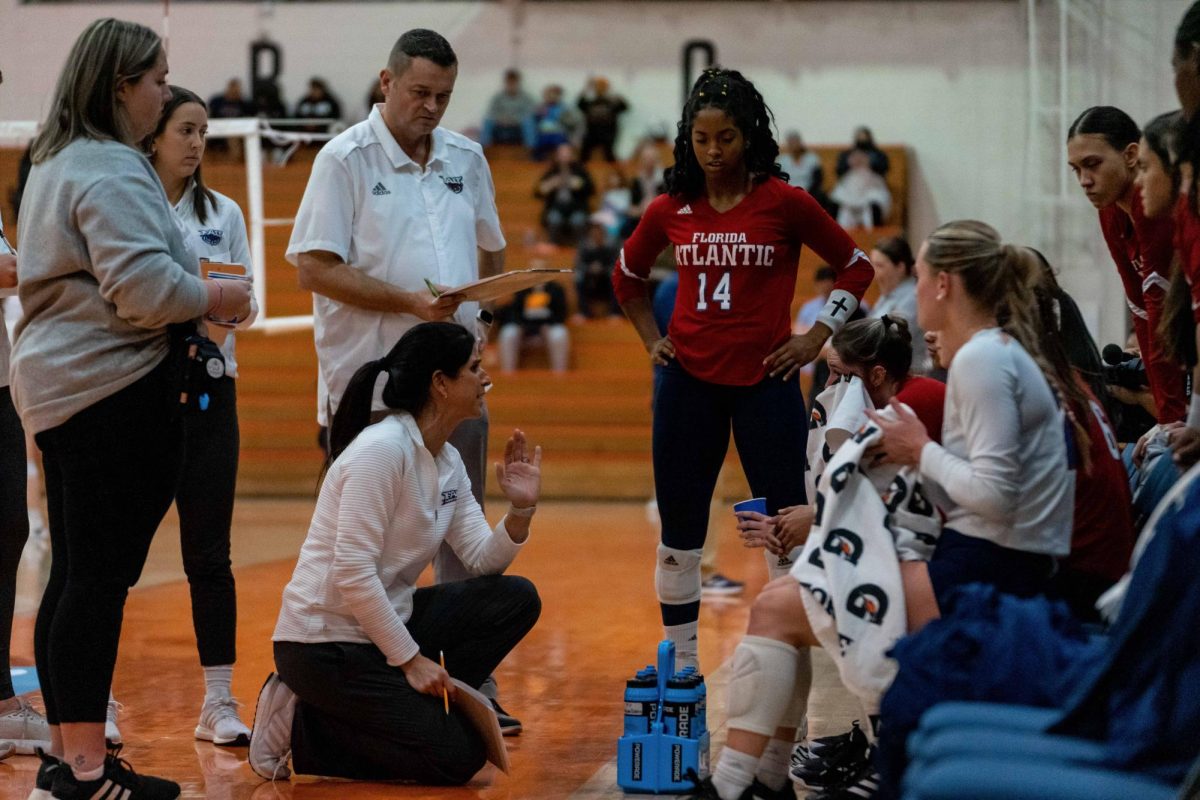 FAU head coach Fernanda Nelson (bottom center) talking to the team during the Owls three-set loss to the UT Arlington Mavericks in the opening round of the NIVC Tournament at Memorial Gym on Friday, Dec. 1, 2023.